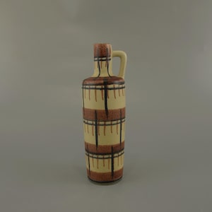 May include: A tall ceramic bottle with a handle. It has a cream-coloured base and brown and black geometric designs. The bottle has a narrow neck and a small handle. The design is vintage and decorative.