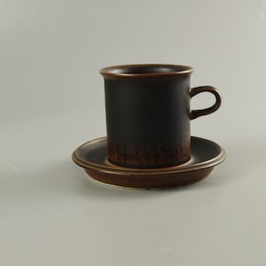 Könnte beinhalten: Ein braunes Keramik-Kaffeetassen-Set. Die Tasse hat eine dunkelbraune Glasur mit einem marmorierten Effekt. Die Untertasse ist hellbraun mit einer glatten Oberfläche.