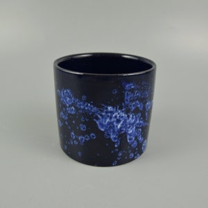 May include: A cylindrical ceramic planter with a dark blue base and a speckled pattern of blue and white. The interior is a solid dark blue. Suitable for indoor or outdoor use.