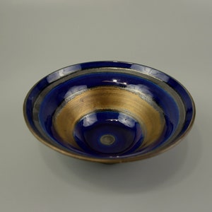 Peut inclure: Un petit bol en céramique bleu et or avec un design en couches. Le bol a une finition brillante et une forme légèrement arrondie.