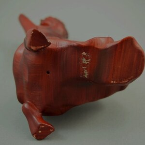 May include: A wooden sculpture of a stylized animal, possibly a dog or a cat, with a reddish-brown finish. The sculpture is standing on its hind legs with its front legs raised.