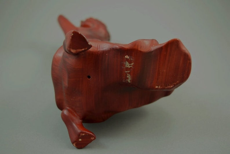 May include: A wooden sculpture of a stylized animal, possibly a dog or a cat, with a reddish-brown finish. The sculpture is standing on its hind legs with its front legs raised.