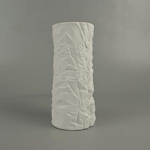 May include: A tall, white ceramic vase with a textured, crinkled surface. The vase has a cylindrical shape and a wide opening. The design gives the vase a unique, artistic look. This decorative vase is suitable for displaying flowers or as a standalone art piece.