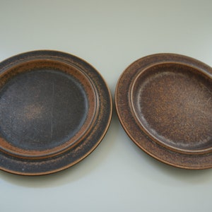 Puede incluir: Dos platos de cerámica marrón con una textura moteada. Los platos tienen un centro marrón oscuro y un borde marrón más claro. Los platos son de forma ovalada y tienen un borde ligeramente elevado.