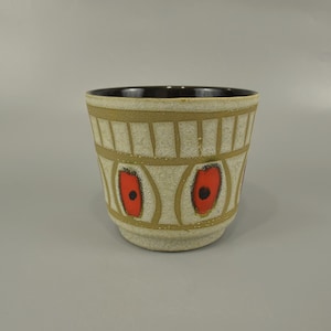 Puede incluir: Un pequeño macetero de cerámica blanca con un borde marrón y un patrón geométrico de óvalos rojos y negros.