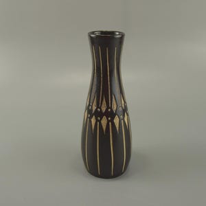 May include: A dark brown vase with a slender, elongated shape. Vertical lines and diamond-shaped accents in a lighter colour adorn the vase's surface. The vase has a narrow neck and a slightly flared base.