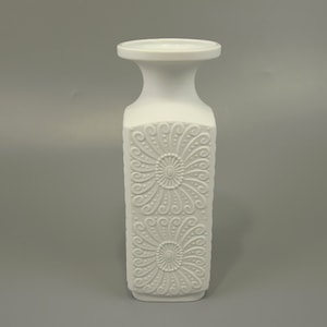Könnte beinhalten: Weiße Porzellanvase mit quadratischem Korpus und einer breiten, runden Öffnung. Die Vase hat ein geprägtes Design aus stilisierten Blumen.