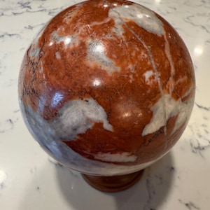 Peut inclure: Un globe terrestre rond en marbre rouge et blanc sur un socle en bois. Le marbre présente un motif tourbillonnant.