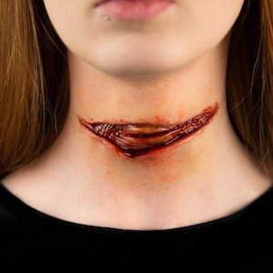 May include: A close-up of a woman's neck with a fake, bloody wound. The wound is a deep cut across the throat, with blood dripping down the skin.