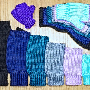 Puede incluir: Una colección de guantes sin dedos de punto en varios colores, incluyendo negro, azul, verde azulado, gris, morado y azul claro. Los guantes están dispuestos en una fila sobre una superficie de madera.