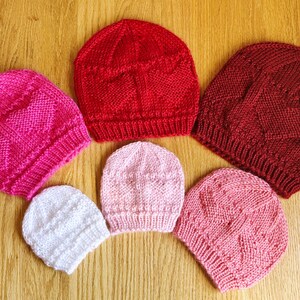 Peut inclure: Cinq bonnets en tricot dans différentes nuances de rose et de rouge. Les bonnets sont tous faits avec un motif de point similaire et ont une couronne arrondie.