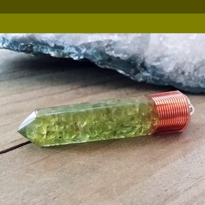 May include: A green crystal point with copper wire wrapped around the top. The crystal is clear and has a green tint. The copper wire is wrapped around the top of the crystal and is secured with a small loop.