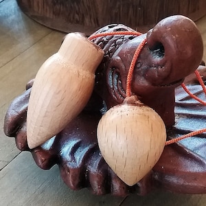 May include: Two wooden pendulum ornaments with a brown ceramic elephant figurine. The ornaments are attached to a red string and are hanging from the elephant's trunk.