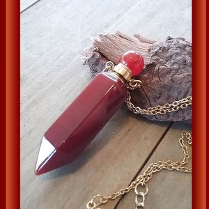 May include: A red carnelian crystal point pendant necklace with a gold chain and a red glass stopper.