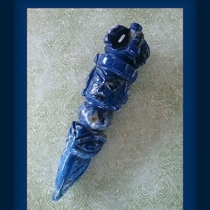 May include: A carved lapis lazuli pendant in the shape of a stylized figure. The pendant is blue with white and gold flecks.