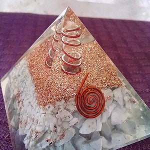 May include: A clear resin pyramid containing a layer of white stone chips, a layer of copper metal shavings, and two copper wire coils embedded inside. A single flat copper wire spiral is attached to the front face of the pyramid structure.
