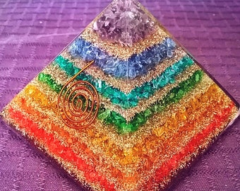 Könnte beinhalten: Eine Regenbogen-Kristallpyramide mit einer Kupferspirale in der Mitte. Die Pyramide besteht aus sieben Schichten verschiedenerfarbiger Kristalle, die die sieben Chakren repräsentieren.