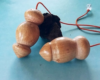 Op de afbeelding: Twee houten pendels met een oranje touwtje en een heldere kristallen kraal. Eén pendel heeft een gestapeld ontwerp, de andere is rond. De pendels zijn lichtbruin en liggen op een lichtblauwe ondergrond.