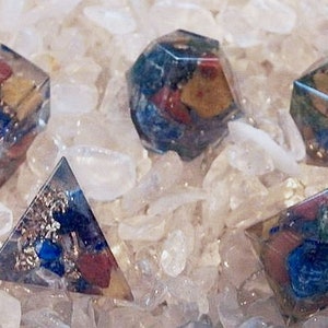 May include: Five clear crystal dice with various colors of stones and minerals inside. The dice are on a bed of white crystal chips.