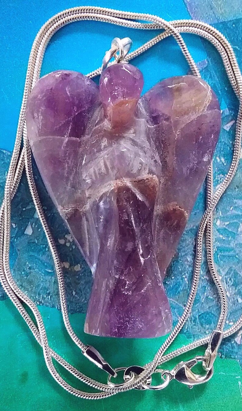 May include: A silver chain necklace with a purple amethyst angel pendant. The angel is carved from a single piece of amethyst and has a detailed design.