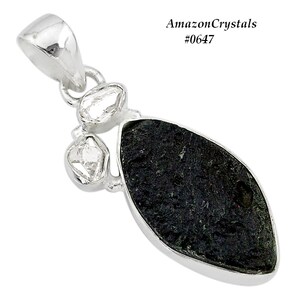 Pode incluir: Um pingente de prata com uma pedra oval de cor verde escura com textura &aacute;spera. A pedra &eacute; cercada por tr&ecirc;s pequenas pedras transparentes e facetadas.
