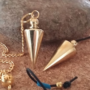 Könnte beinhalten: Zwei goldfarbene Metallpendel mit Ketten. Ein Pendel hat eine goldene Kette und das andere eine schwarze Schnur.