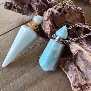 May include: Two pointed gemstone pendants with metal caps and chains. One pendant is a smooth, pale blue-green cone with a gold-tone cap. The other is a faceted, vibrant teal-green hexagonal prism with a silver-tone cap and a matching metal chain.