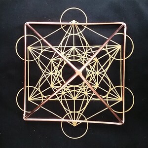 K&ouml;nnte beinhalten: Eine geometrische Form aus Kupferdraht mit einem goldenen Design im Inneren. Die Form ist ein W&uuml;rfel mit einer Pyramide auf der Oberseite. Das Design im Inneren ist ein komplexes Muster aus Kreisen und Linien.