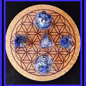 May include: Five blue lapis lazuli gemstone dice on a cork coaster with a flower of life pattern. The dice are in the shapes of a cube, a tetrahedron, a dodecahedron, an icosahedron, and an octahedron.