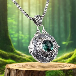 May include: A silver pendant necklace with an ornate, engraved design. The pendant features a large, faceted, emerald-green gemstone set in a detailed, circular frame. The necklace hangs from a silver chain, showcasing a vintage or antique aesthetic.