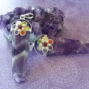 May include: Two amethyst crystal pendants with silver settings and colorful gemstone accents. The pendants are displayed on a bed of amethyst crystals.
