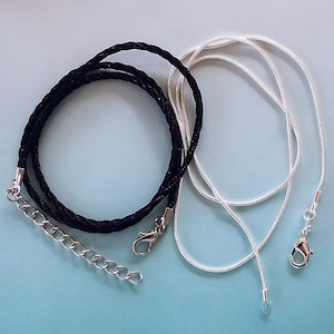 May include: Two necklaces, one black braided cord with a silver clasp and one silver chain.