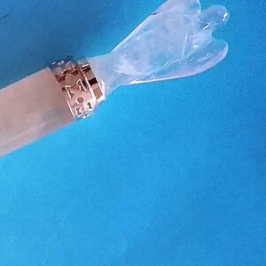 May include: A clear crystal angel wand with a decorative gold-coloured band. The wand has a light-coloured handle against a bright blue background. The angel figure has outstretched wings.