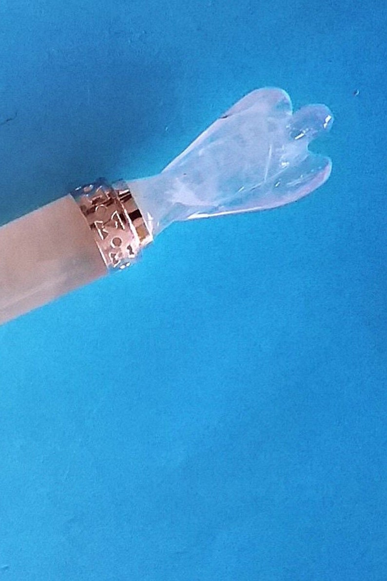 May include: A clear crystal angel wand with a decorative gold-coloured band. The wand has a light-coloured handle against a bright blue background. The angel figure has outstretched wings.