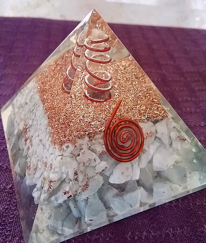 May include: A clear resin pyramid containing a layer of white stone chips, a layer of copper metal shavings, and two copper wire coils embedded inside. A single flat copper wire spiral is attached to the front face of the pyramid structure.