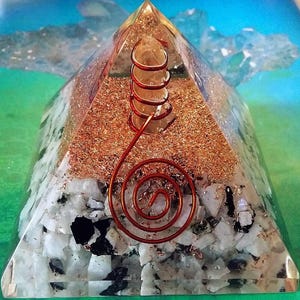 May include: A clear resin pyramid containing a central quartz crystal point wrapped in a copper wire coil. The base layer features white and black stone fragments, while the upper section is filled with fine copper shavings and a spiral wire.