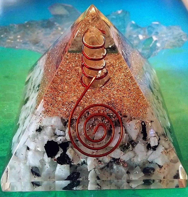 May include: A clear resin pyramid containing a central quartz crystal point wrapped in a copper wire coil. The base layer features white and black stone fragments, while the upper section is filled with fine copper shavings and a spiral wire.