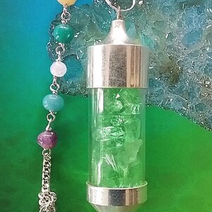 May include: A silver pendulum with a clear glass vial filled with green crystals. The pendulum is attached to a silver chain with a variety of colored beads.