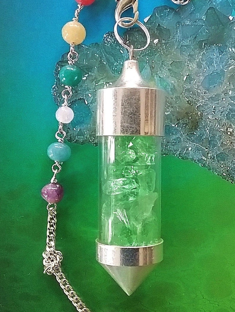 May include: A silver pendulum with a clear glass vial filled with green crystals. The pendulum is attached to a silver chain with a variety of colored beads.
