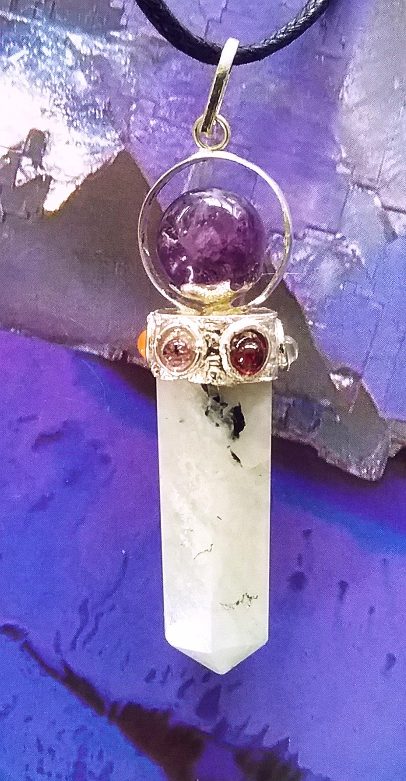 May include: A silver pendant with a clear crystal point and a round amethyst stone in a silver cage. The pendant is on a black cord and is surrounded by a purple background.