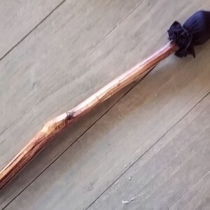 May include: A long, slender wooden wand featuring a natural, light brown bark texture and a smooth, polished finish. At one end, a dark navy blue fabric pouch is gathered and secured with a matching fabric tie, creating a rounded, bulbous tip.