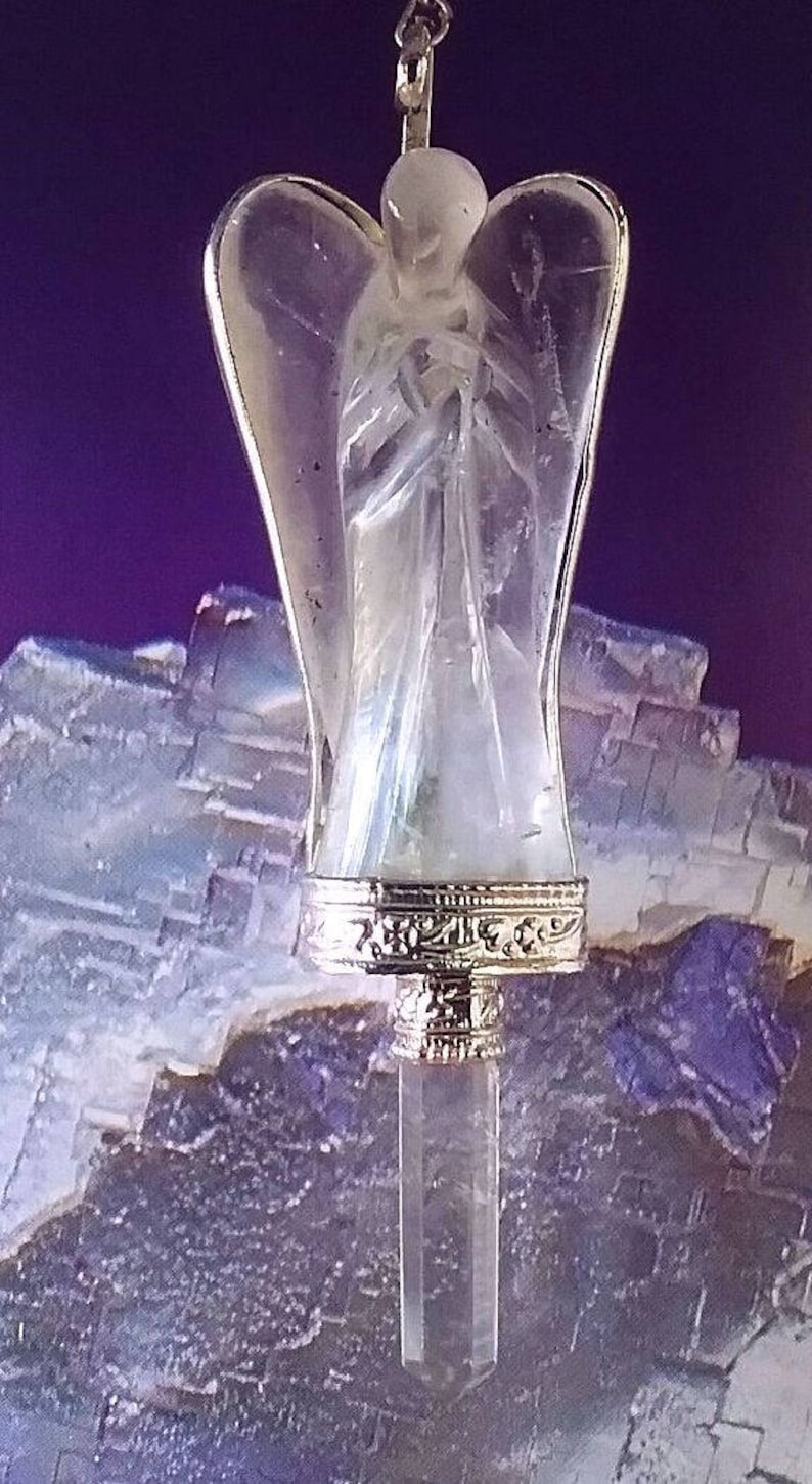 May include: A clear crystal angel pendant with silver accents. The angel is holding its hands together in prayer. The pendant is hanging from a silver chain.