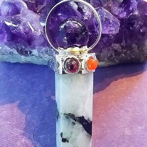 May include: A silver pendant with a clear crystal point, surrounded by a circle of amethyst and four smaller stones in red, orange, blue, and purple. The pendant is hanging from a black cord.
