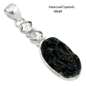 Pode incluir: Um pingente de prata com uma pedra preta de forma oval e tr&ecirc;s pedras transparentes facetadas. O pingente est&aacute; sobre um fundo branco. AmazonCrystals #0649