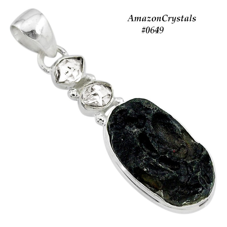 Pode incluir: Um pingente de prata com uma pedra preta de forma oval e tr&ecirc;s pedras transparentes facetadas. O pingente est&aacute; sobre um fundo branco. AmazonCrystals #0649