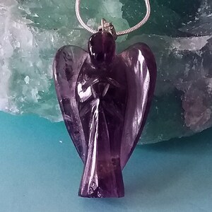 May include: A purple amethyst angel pendant carved from a single piece of crystal. The angel is wearing a silver chain.