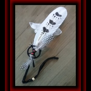 May include: A white feather with black spots and a black and red beaded dreamcatcher. The feather is attached to a black cord.