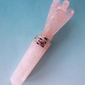 May include: A pink rose quartz angel wing wand with a silver setting and a red gemstone accent.