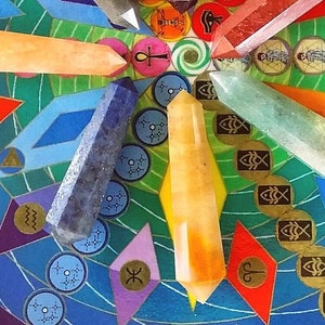 May include: Five polished crystal points in orange, dark blue, yellow, clear, and reddish-pink arranged on a circular board featuring colorful geometric patterns, zodiac symbols, and various icons including an ankh and fish.