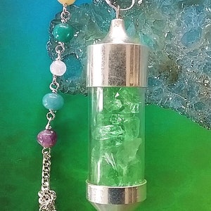 May include: A silver pendulum with a clear glass vial filled with green crystals. The pendulum is attached to a silver chain with a clear crystal at the end and a series of colorful beads.